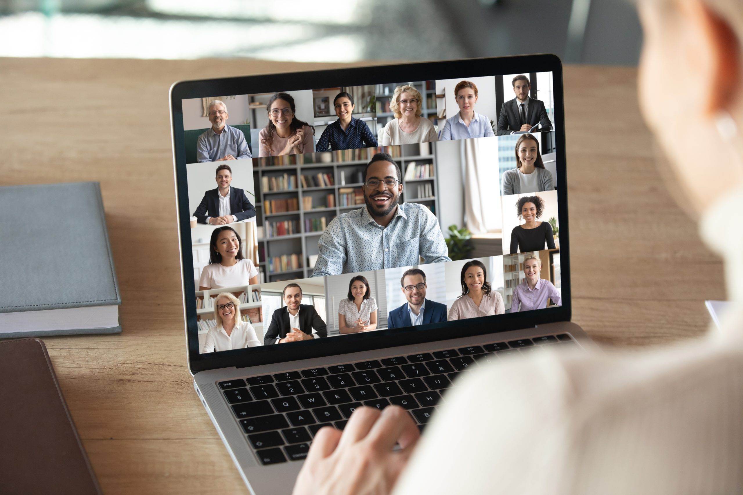 A man looks at a laptop featuring a gallerry-style Zoom screen for a digital meeting.