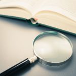 An open book on a table beside a magnifying glass