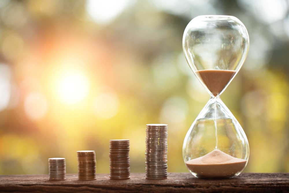 Piles of stacked coins next to an hourglass against a blurred sunset background.