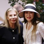 Yasmin Aga Khan, in black, stands to the left of Lucia Hwong Gordon, in white with a white hat.